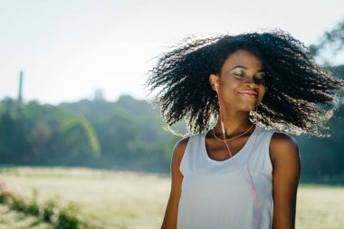 Kapalı eas ve yeşil göz gölgeler ile büyüleyici Afrikalı kız kıvırcık saçları sallayarak ve onun kulaklık açık müzik keyfi.