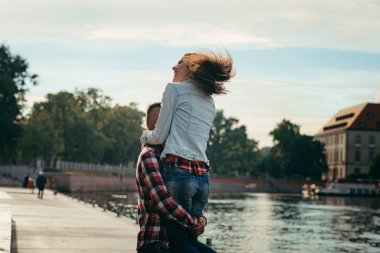 Genç adam arka plan Polonya Nehri'nin, neşeli gülen güzel kız kaldırma. Arkadan Görünüm.