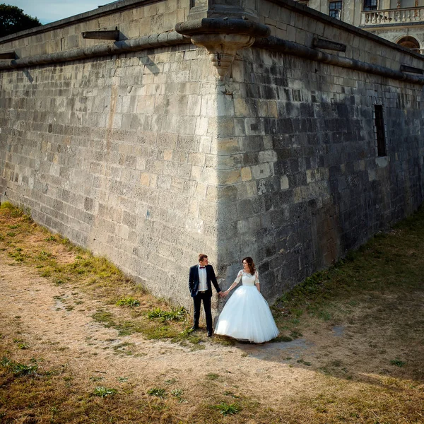 Sposi si si tengono per mano mentre in piedi in un angolo delle enormi mura del vecchio castello barocco . — Foto Stock