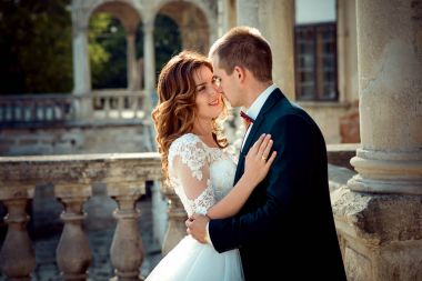 Romantic outdoor portrait of the beautiful happy newlywed couple tenderly rubbing noses. clipart