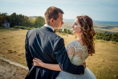 Yakın çekim geri görüntülemek, sarılma ve muhteşem manzaralı arka plan birbirine bakarak sevimli gülümseyen yeni evliler.