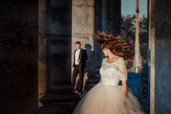 Affascinante sposa felice sta scuotendo i capelli ricci zenzero sullo sfondo sfocato dello sposo vicino al vecchio castello . — Foto Stock