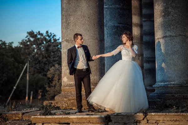 Romantico ritratto di nozze all'aperto della splendida coppia di sposi che si tiene per mano mentre si trova sulle scale del vecchio castello durante il tramonto . — Foto Stock