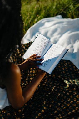 Afrika omuz üzerinden bakmak. Genç kadın bir piknik üzerinde kitap okuyor. Arkadan Görünüm. Yüzü olmayan.