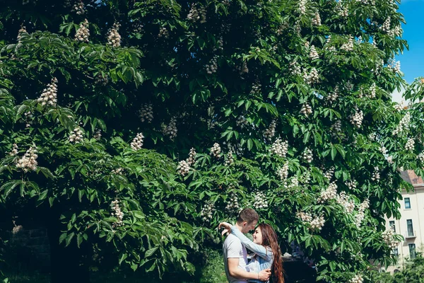 Retrato do casal muito sorridente apaixonado abraçando ternamente perto da árvore florescente verde em Budapeste, Hungria . — Fotografia de Stock