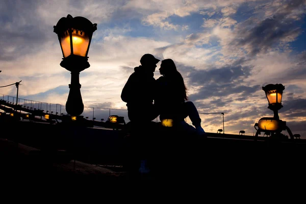 Budapeşte, Macaristan için yıldırım sokak lambası yakın zincir köprü üzerinde oturan sevgi dolu çift siluet romantik portresi. Güzel renkli gökyüzü görünümü. — Stok fotoğraf