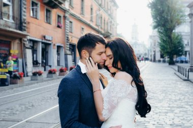 Sarılma büyüleyici yeni evliler romantik açık portresi. Güzel esmer gelin şefkatle damadın yüzünü okşayarak.