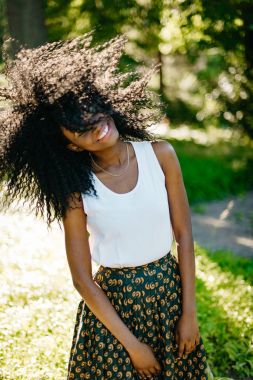 Pozitif ile güzel büyüleyici Afrikalı kız portresi gülümsemek güneşli ormanda karanlık kıvırcık saçları sallama emotionaly.