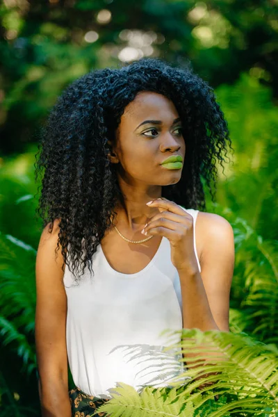 Retrato de meio-comprimento da jovem menina africana aforable com batom verde e sombras de olhos olhando para o lado no jardim samambaia . — Fotografia de Stock