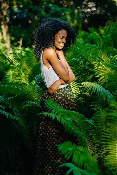 The attractive african girl with green make-up, charming smile and in stylish clothing is posing in the fern garden.