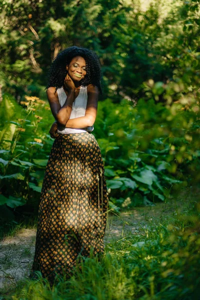 Retrato completo da linda menina africana com maquiagem verde em roupas elegantes desfrutando da natureza na floresta verde . — Fotografia de Stock