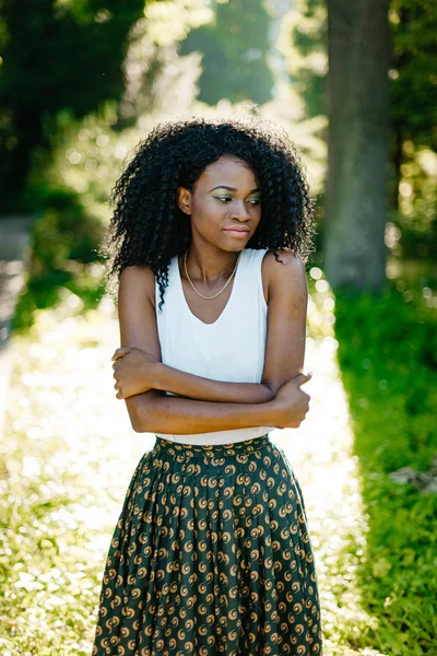 Retrato de media longitud de la tierna y hermosa chica africana con sombras de ojos verdes mirando a un lado el soleado fondo verde borroso . — Foto de Stock