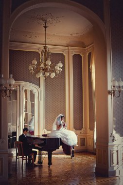 Zengin opld odasında güzel şık çiftin düğün portre. Sevimli gelini üzerinde oturuyor iken yakışıklı damat piyano çalıyor.