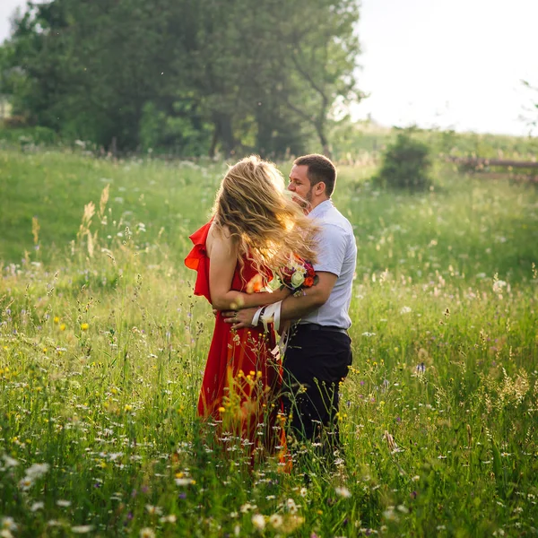 Slunné venkovní portrét šťastné usmívající se pár objímat na rozkvetlé louce. Vítr se pohybuje blond kudrnaté vlasy ženy. — Stock fotografie