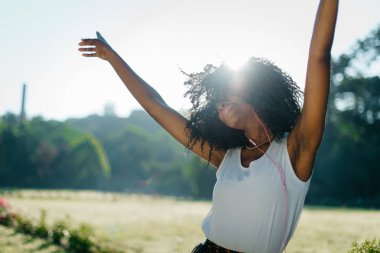 Güneşli portre alanında. Dans ve müzik kulaklığı tadını çıkarırken kıvırcık saçları ve eller Afrikalı kız sallayarak Emotionaly.