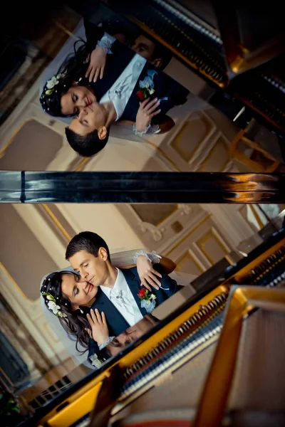 Sensitive portrait of the attractive bride hugging her lover back. The reflection on the piano. — Stock Photo, Image