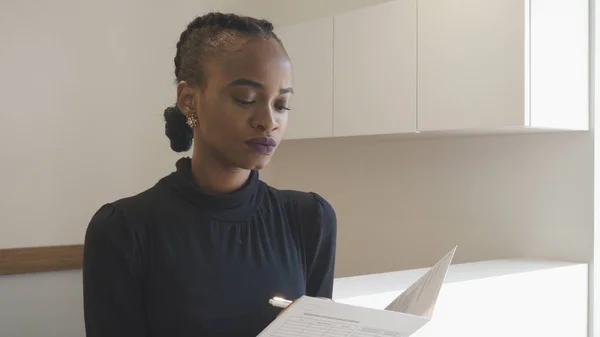 Serious afro-american woman is filling in the form. The beautiful brunette with natural make-up working at the repcetion. — Stock Photo, Image