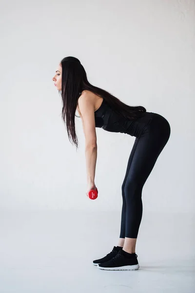 Plnohodnotné boční pohled sportovní bruneta ohyb s činkami v rukou ve studiu. — Stock fotografie