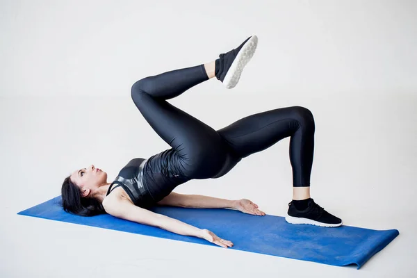 Tutorials for cardio beginners. The attractive sportive brunette is doing crab kicks while lying on the exercise mat in the white studio. — Stock Photo, Image