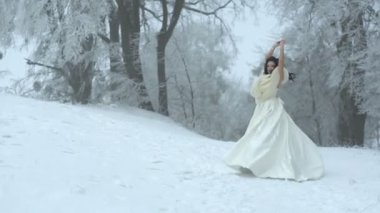 Siyah kıvırcık saçlı uzun gelinlikle çok güzel şık genç gelinle karlı ormanda yuvarlak dönüyor.