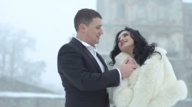 Romantik düğün portre elele ve şefkatle birbirleriyle gözlere bakmak yeni evli genç mutlu çiftin. Yakışıklı damat yavaşça onun sevgilisi burnuna kar yağışı sırasında öpüyor.