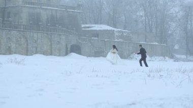 Mutlu güzel yeni evliler üzerinde çalışırken, yuvarlak dönen eski castle yakınındaki karlı çayır eğleniyorlar. Çekici gelin kar düşüyor.