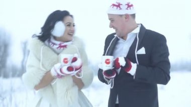 Gülen ve clincking bardak çay ya da kahve karlı çayır üzerinde mutlu gülümseyen yeni evliler komik eldiven ve şapka vardır.