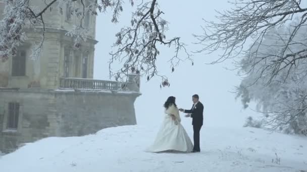 Dansande nygift par på snöiga ängen nära det gamla huset. Attraktiva bruden snurrar runt. — Stockvideo