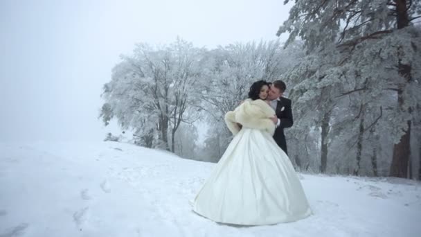 The full-length sensual portrait of the handsome groom softly hugging his lover back, correcting her fur coat and kissing while standing on the snowy meadow. — Stock Video