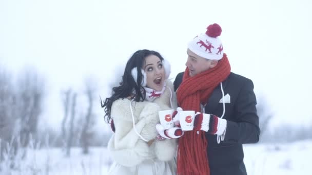 Happy newlyweds are having fun, laughing, making funny faces and drinking tea or coffee being dressed in wedding clothes, funny gloves and hats. Winter time. — Stock Video