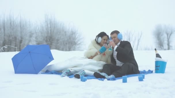 Feliz recién casados se ríen mientras beben champán durante su picnic de invierno de boda en color azul decorado con paraguas y velas . — Vídeos de Stock