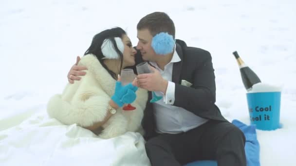 Retrato de cerca de los alegres y hermosos recién casados besándose suavemente mientras sostienen las copas durante su picnic de invierno al fondo del champán en cubo . — Vídeo de stock