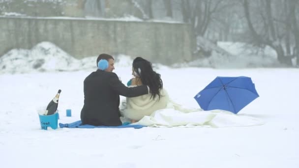 Zadní pohled na šťastné rozkošný novomanželé mluví a řinčí poháry v sedle potíže během své zimní piknik v modré barvě. — Stock video