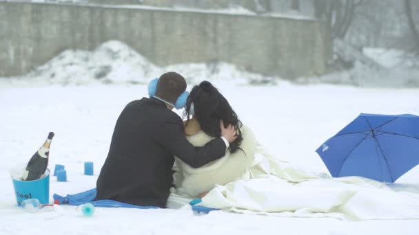 Newlyweds during their winter picnic in blue colour. Back view of the couple tenderly hugging and enjoying the snowfall. — Stock Video