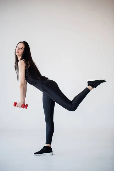 Smiling sportwoman is doing leg exercises while holding the dumbbells. Studio location. — Stock Photo, Image