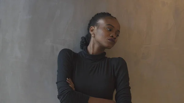 Deprimida hermosa mujer africana con coletas, lápiz labial púrpura y brazos cruzados se apoya en la pared gris y mirando a un lado . — Foto de Stock