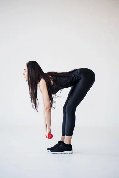 Beautiful athletic sportwoman is doing exercises with the red dumbbells in the studio. Side view. — Stock Photo, Image