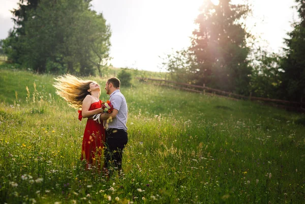 Vacation on the sunny meadow of the happy hugging couple in love. The charming young girl is shaking her long curly blonde hair. — Stock Photo, Image