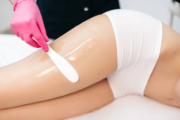 Depilation and Skin care. The beautician is preparing woman in lingerie to laser hair removal by applying the cream with the wax stick in beauty salon. No face.