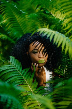 Yakın çekim yeşil ruj ve şefkatle yüzü yeşil ferns tarafından çevrili süre dokunaklı kaptırdın ile genç ve güzel Afrikalı kız portresi.