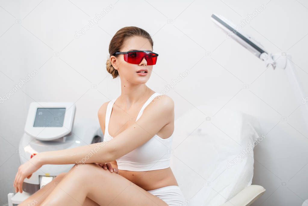 Portrait of attractive young fresh healthy woman in white lingerie, natural make-up and red safety goggles sitting on the beauty salon chair and looking aside.