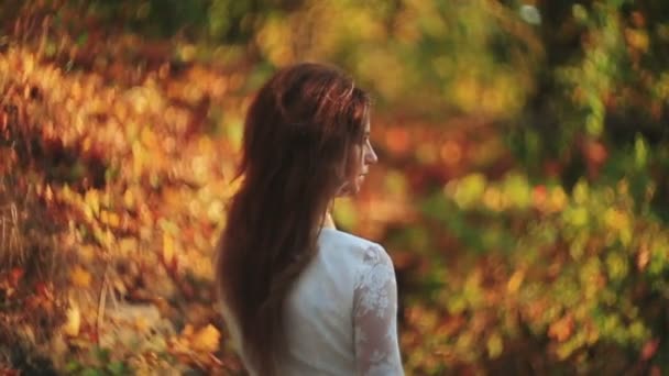 Vista posterior de la joven morena de pelo largo en el vestido blanco disfrutando de la naturaleza en el bosque de otoño . — Vídeo de stock