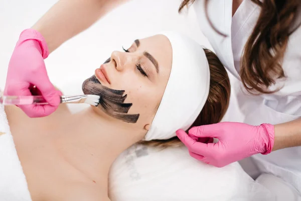 Руки косметолога наносят черную маску с кистью на лицо красивой женщины с натуральным макияжем в спа-салоне . — стоковое фото