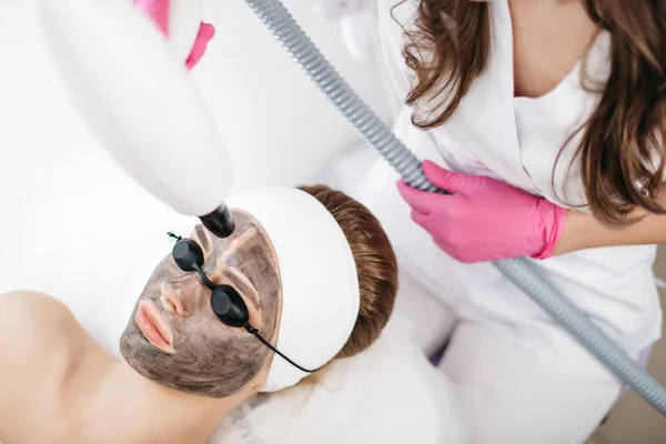Молодая очаровательная женщина в масках и защитных очках получает лазерное лечение лица и ультразвука в профессиональном салоне красоты . — стоковое фото