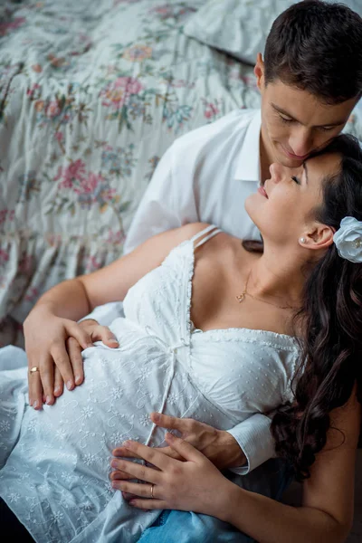 Gevoelige familie indoor portret van de knappe man knuffelen zijn mooie zwangere vrouw terug. — Stockfoto