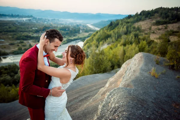 Adorables recién casados alegres se abrazan en el fondo del hermoso paisaje. El retrato emocional de la boda . —  Fotos de Stock