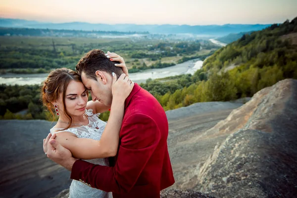 Свадебный наружный портрет. Красивые молодожены нежно обнимаются на фоне великолепного пейзажа во время заката . — стоковое фото