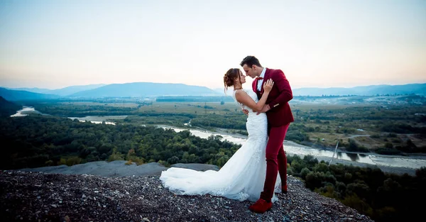 在风景的背景下, 可爱的新婚夫妇拥抱在山的 adge 的全长婚礼拍摄. — 图库照片