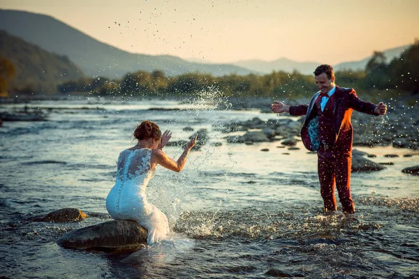 Емоційна зовнішньої весілля портрет щасливі красиві усміхнений молодят гра бризки води, маючи весело Sunset гори краєвид. — стокове фото