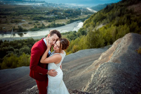 Retrato sensível do adorável casal recém-casado abraçando no fundo da magnífica paisagem durante o pôr do sol . — Fotografia de Stock